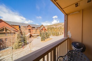 A balcony with a view of a lodge building, a barbecue grill, and a parking area with trees.