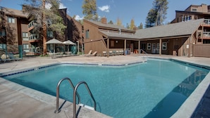 A swimming pool with a metal ladder, lounge chairs, and umbrellas in a resort setting.