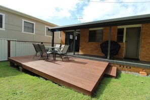 A covered patio with a wooden deck, a table with chairs, and a barbecue grill. - Breakaway, 11 Scott Street, (Crescent Head)