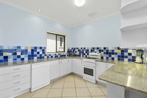 A kitchen with white cabinets, a stove, a sink, and a window with blinds. - Cooinda, 17 Dulconghi Street, (Crescent Head)