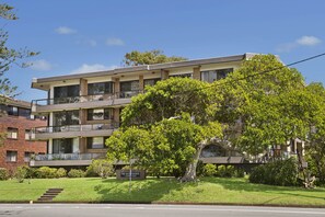 A multi-story building with balconies, a sign reading "The Quarterdeck 7th Street", and a well-maintained lawn. - Quarterdeck 11, 7 Stewart Street, (Port Macquarie)