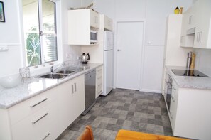 A modern kitchen with white cabinetry, stainless steel appliances, and a checkered floor. - Fleur Cottage, 7 Willow Street, (Crescent Head)