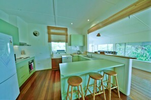 A modern kitchen with a central island, wooden stools, and a view of greenery outside. - Rosemaree, 24 East Street, (Crescent Head)