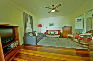 A living room with a television, sofa, coffee table, and a ceiling fan. - Rosemaree, 24 East Street, (Crescent Head)