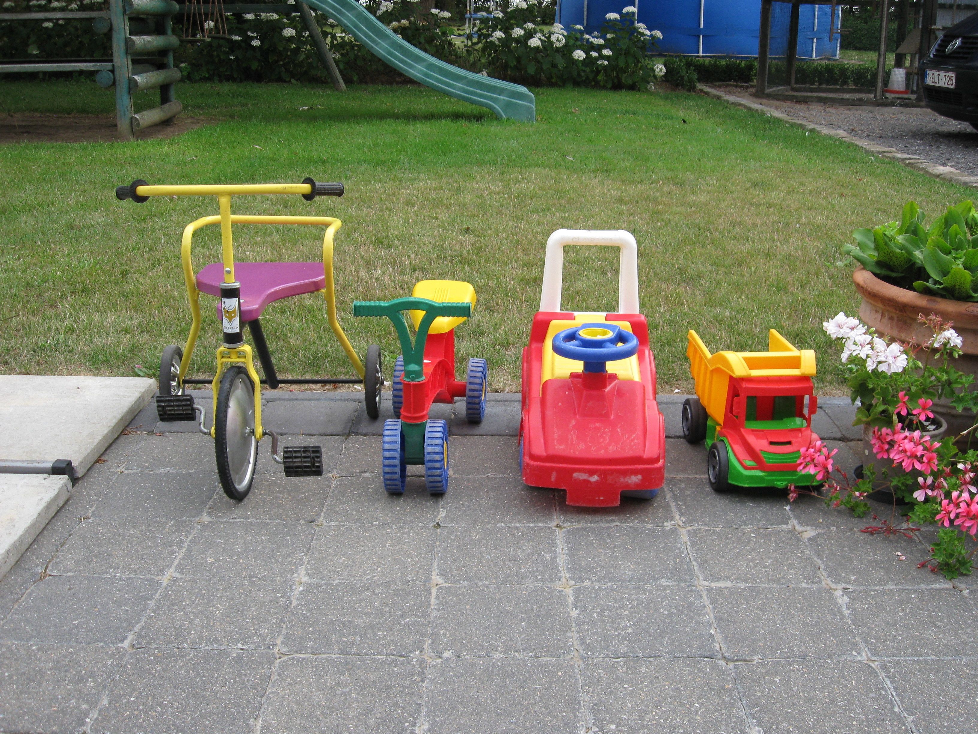 Een kinderspeelplaats met een driewieler, een speelgoedauto en een trekker.