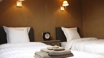 Una habitació d'hotel amb dos llits, cadascun amb un coixí etiquetat "Hooghe Licht", una taula de nit amb un rellotge i dues làmpades penjades a la paret.