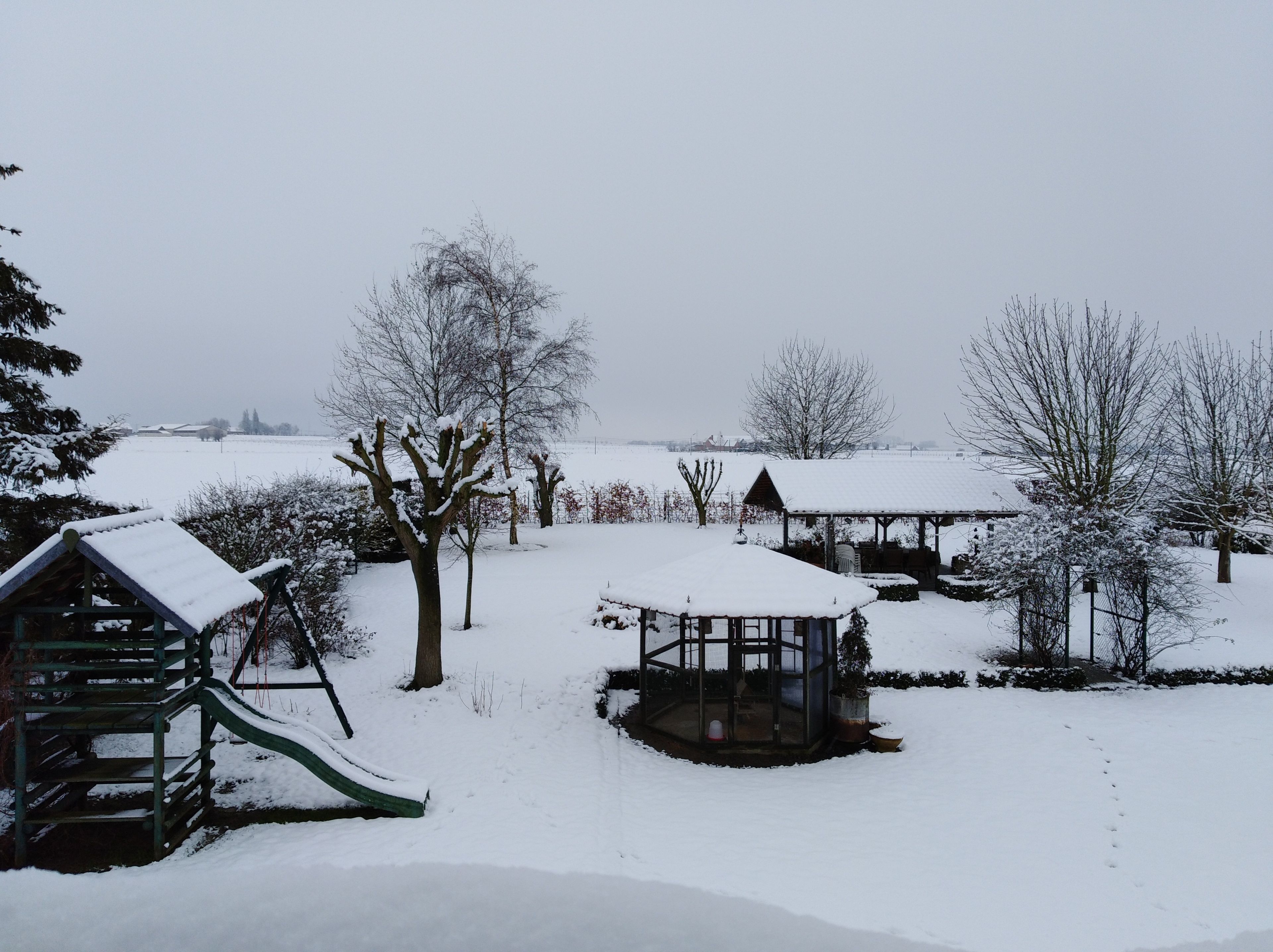 A snow-covered park with a playground, a gazebo, and bare trees.