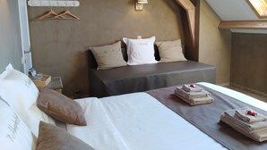 Une chambre à coucher avec un lit, des oreillers, une table de chevet, une pile de serviettes et un luminaire fixé au mur.