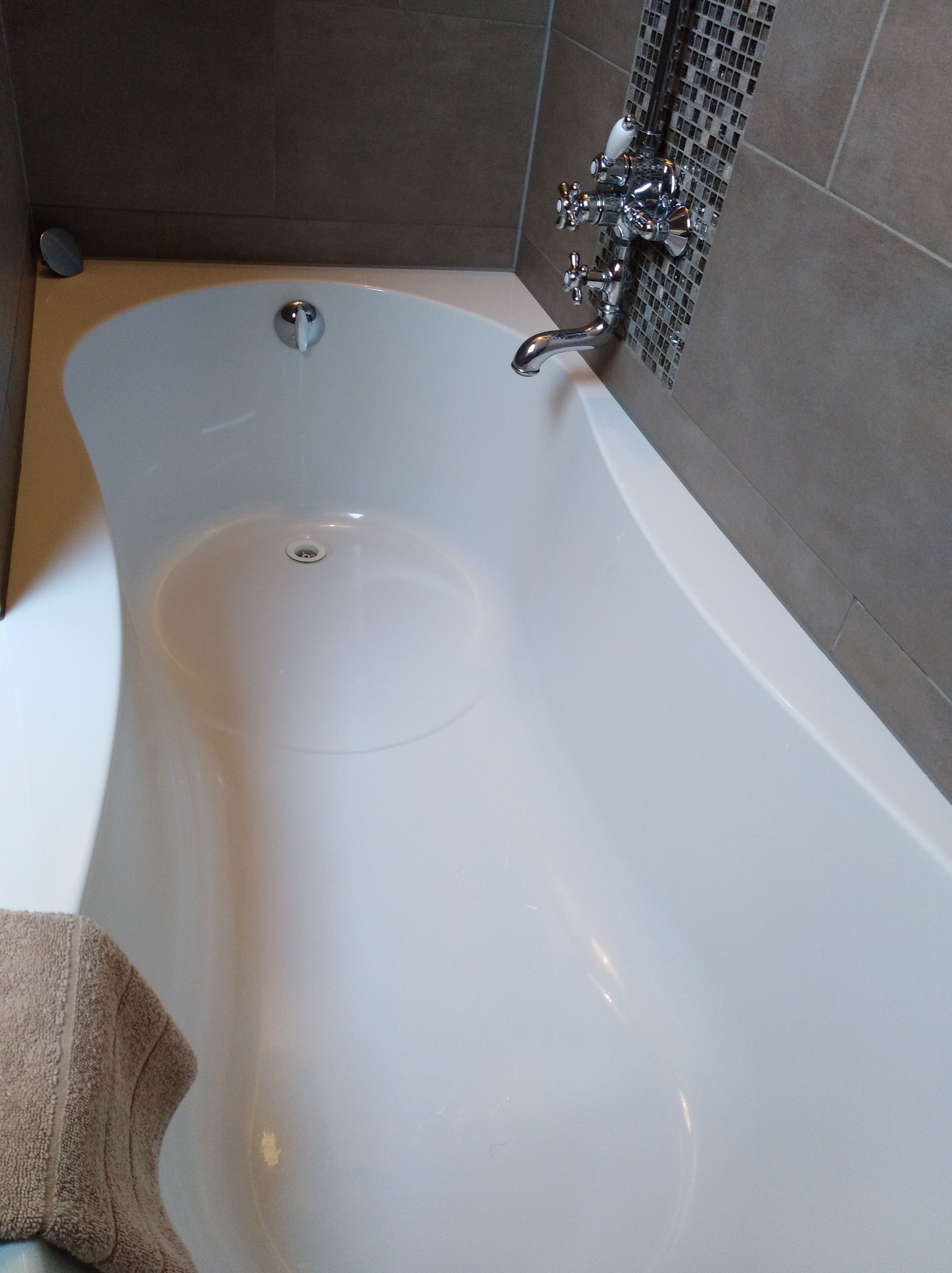 Une baignoire blanche, dotée d’un seul robinet et d’un drain, placée contre un mur carrelé.
