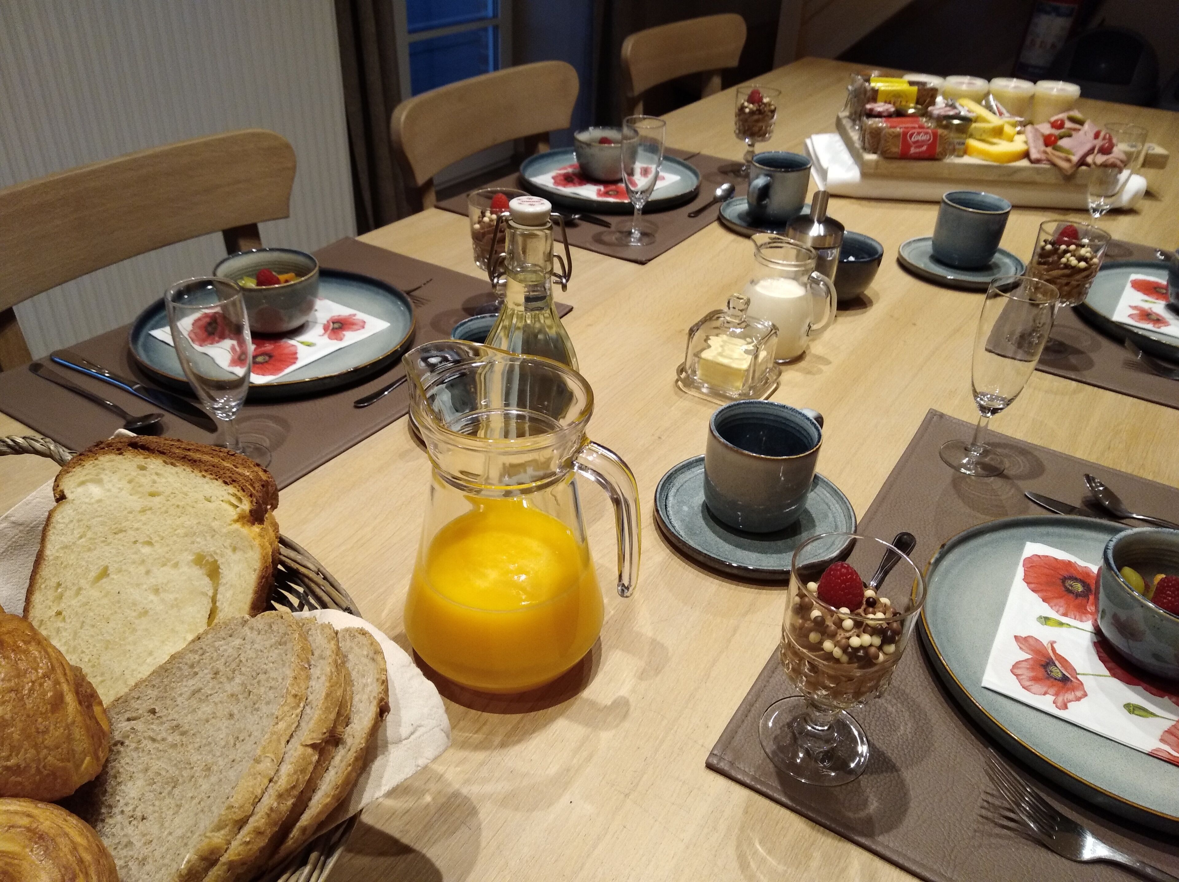A dining table set with various breakfast items including bread, a pitcher of orange juice, and a dessert glass.