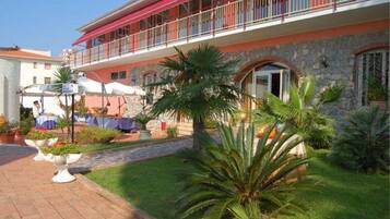 A hotel with a red balcony, stone facade, and a paved courtyard with potted plants.