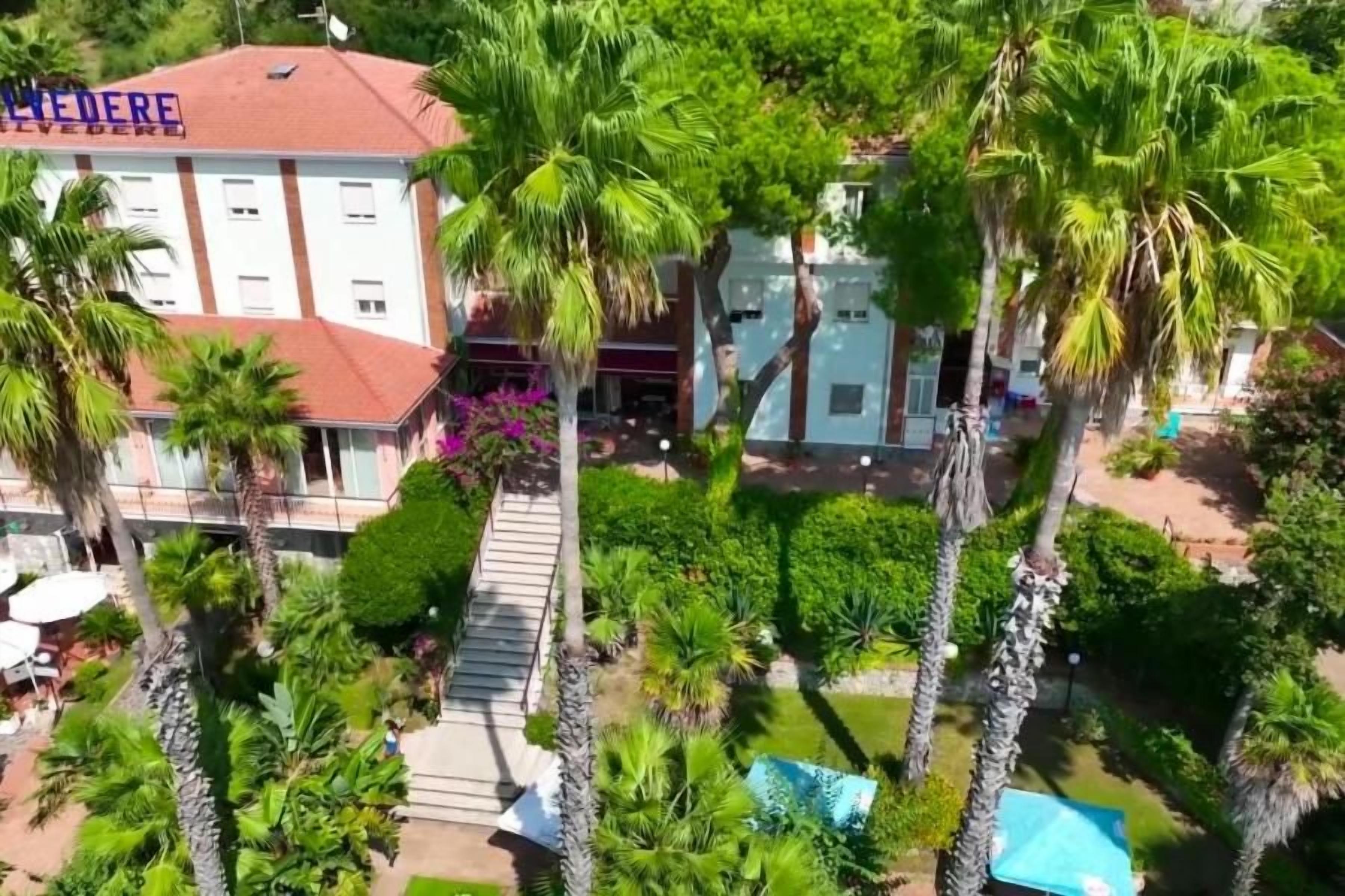 Un hotel con tetto rosso, circondato da palme e un giardino curato.