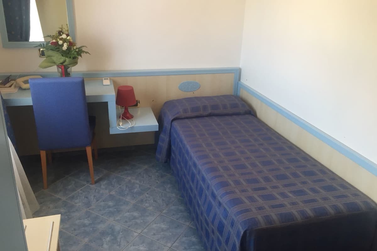 Une petite pièce, de taille modeste, comprenant un lit simple, un bureau, une chaise et un miroir.
