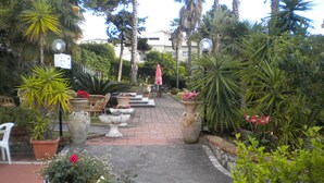 Une cour intérieure agrémentée de plantes en pot, de mobilier d’extérieur et d’un chemin menant à un bâtiment.