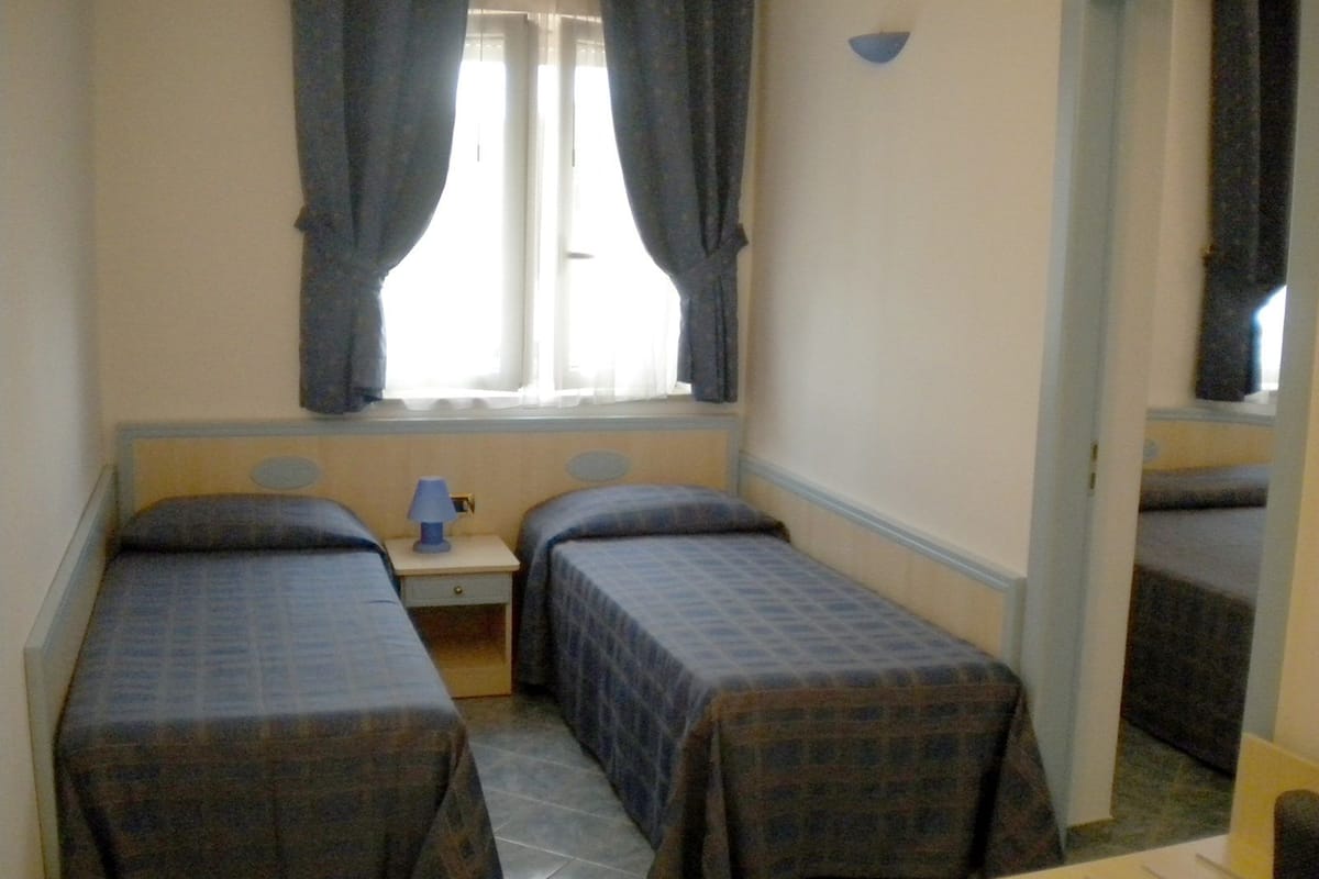Une petite pièce simple, avec deux lits, une table de chevet et une fenêtre avec des rideaux.