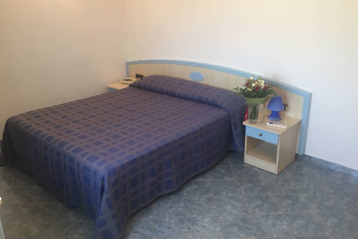 Une chambre à coucher avec un lit, une table de chevet, une lampe et un vase de fleurs.