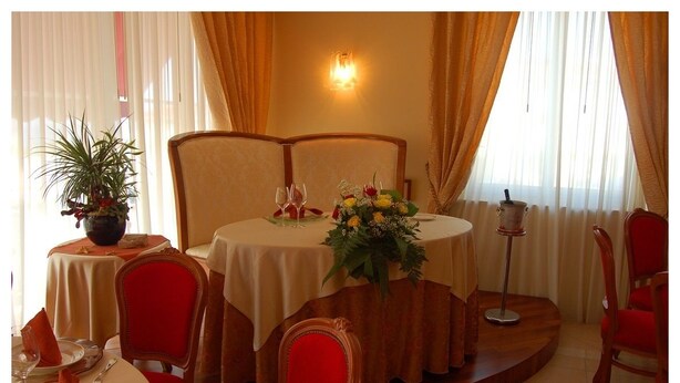 Un coin repas avec une table ronde, des chaises à revêtement rouge, une plante en pot et un vase rempli de fleurs.