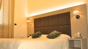 Una camera d'albergo con un letto grande, una testiera imbottita, due abat-jour e un comodino con un oggetto decorativo.