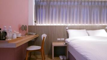 A hotel room with a bed, a desk with a chair, a nightstand, a mirror, and a window with curtains.
