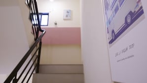 Una escalera con barandilla negra que lleva a un rellano con un cuadro enmarco y un cartel.
