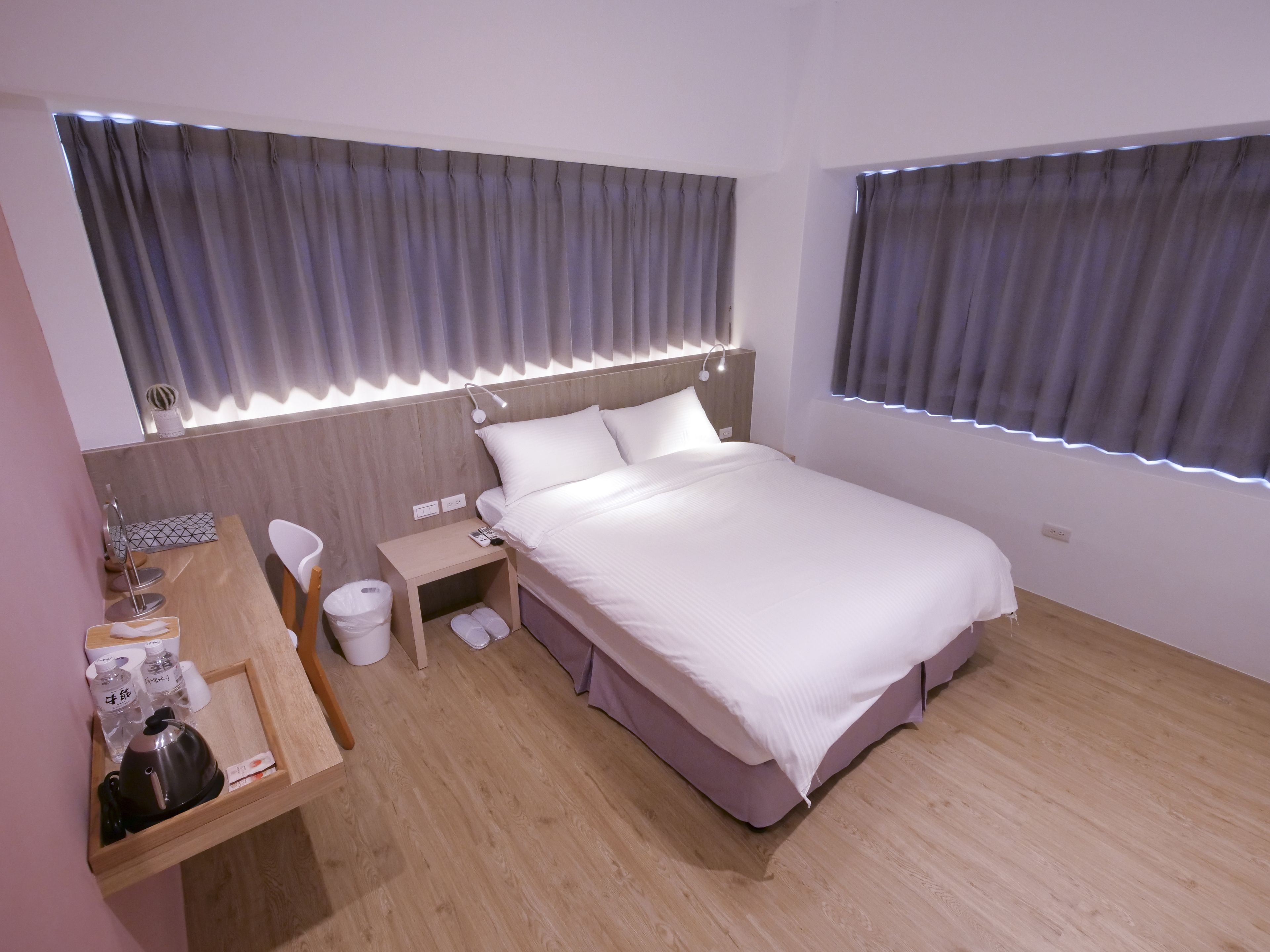 A modern hotel room with a large bed, bedside table, and a small desk.