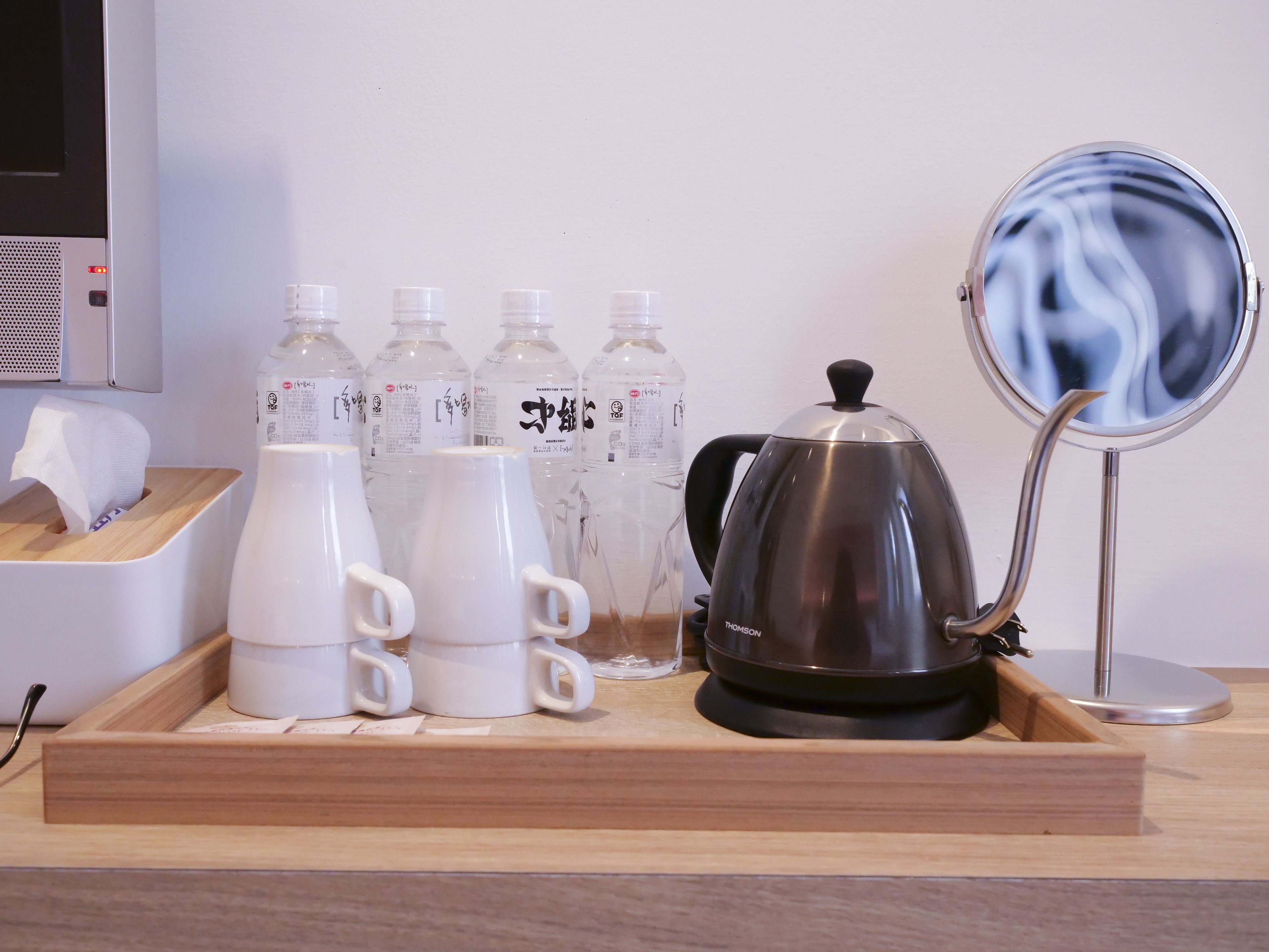 A tray with white cups, a stainless steel kettle, and water bottles on a wooden table.