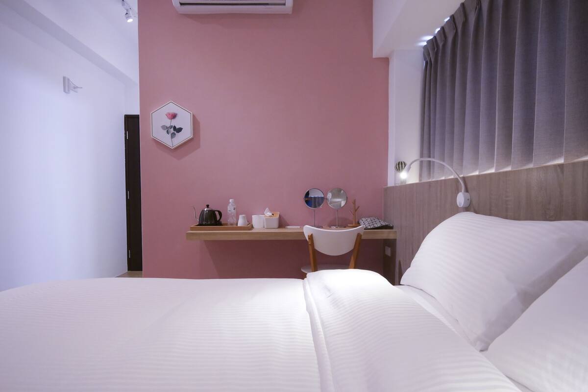 A hotel room with a bed, a desk with a chair, a small table with a kettle, cups, and a tissue box.
