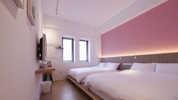 Un dormitorio moderno con dos camas, suelo de madera, una pared de acento rosa y un televisor montado en la pared.