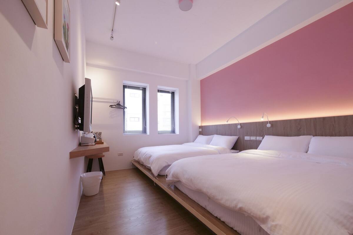A modern bedroom with two beds, a wooden floor, a pink accent wall, and a wall-mounted TV.