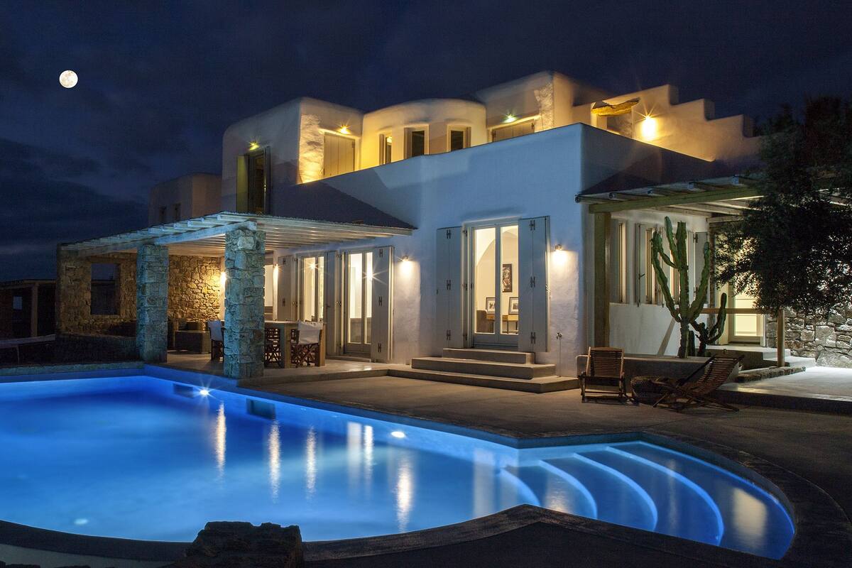 Une maison moderne avec une piscine, des piliers en pierre et une lune dans le ciel.