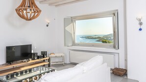 A modern room with a large window, a flat-screen TV, and a wooden ceiling light fixture. - DreamLike Villas Mykonos (Mykonos)