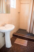 Un baño con un lavamanos pedestal blanco, una ducha con piso de azulejos y una alfombra a rayas en el suelo.