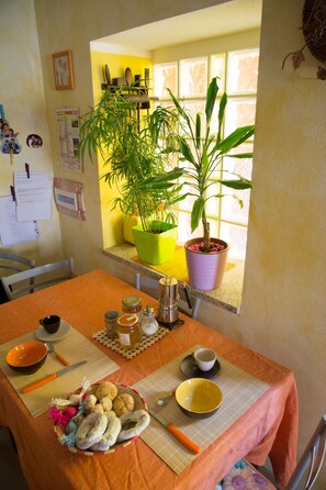A dining area with a table set for two, featuring a yellow bowl, a green plant, and a potted plant by the window. - B&B Annalu (Guspini)