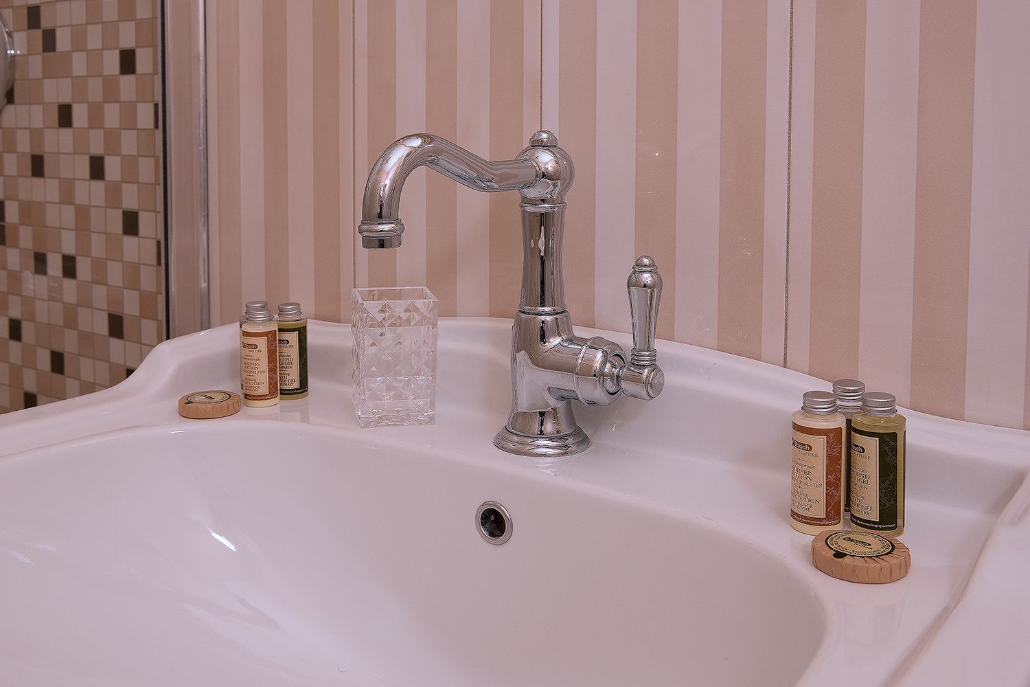 A bathroom sink with a chrome faucet, a glass container, and several bottles of toiletries.