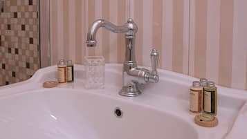 A bathroom sink with a chrome faucet, a glass container, and several bottles of toiletries.