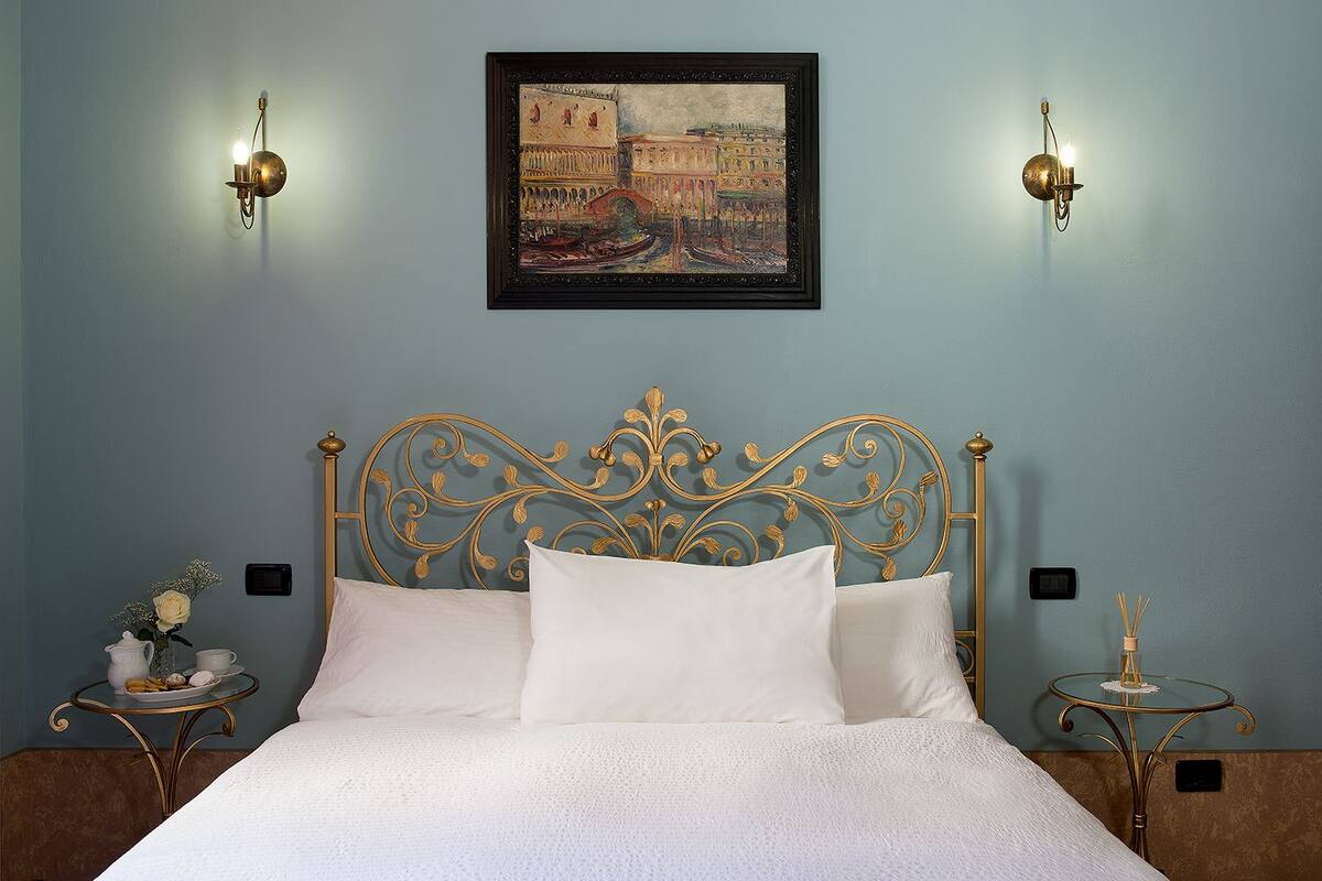A bedroom with a bed, a wall-mounted painting, and two wall sconces.