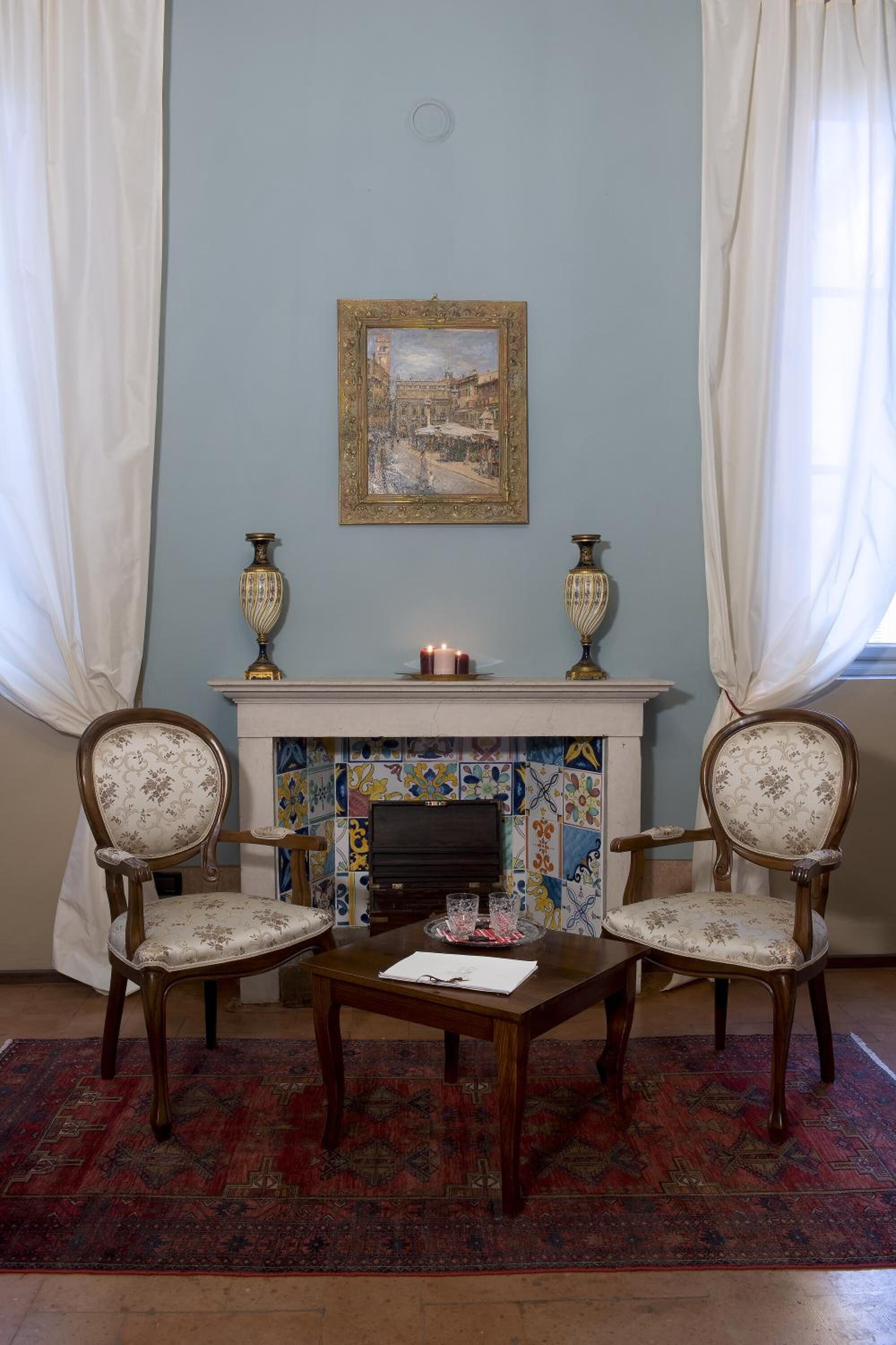 Una habitación con chimenea, dos sillas, una mesa y un cuadro en la pared.