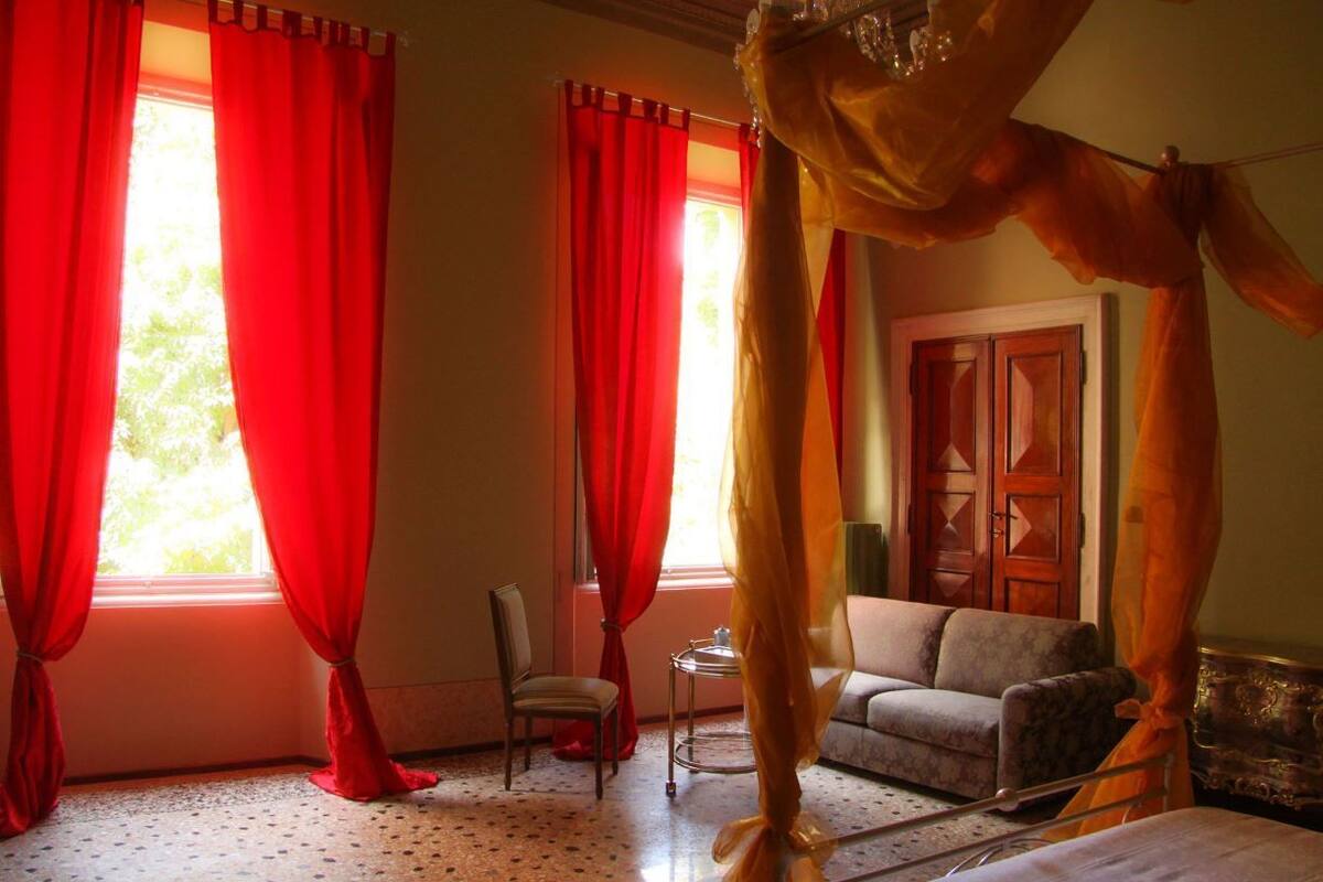 A room with a canopy bed, red curtains, a sofa, and a wooden door.