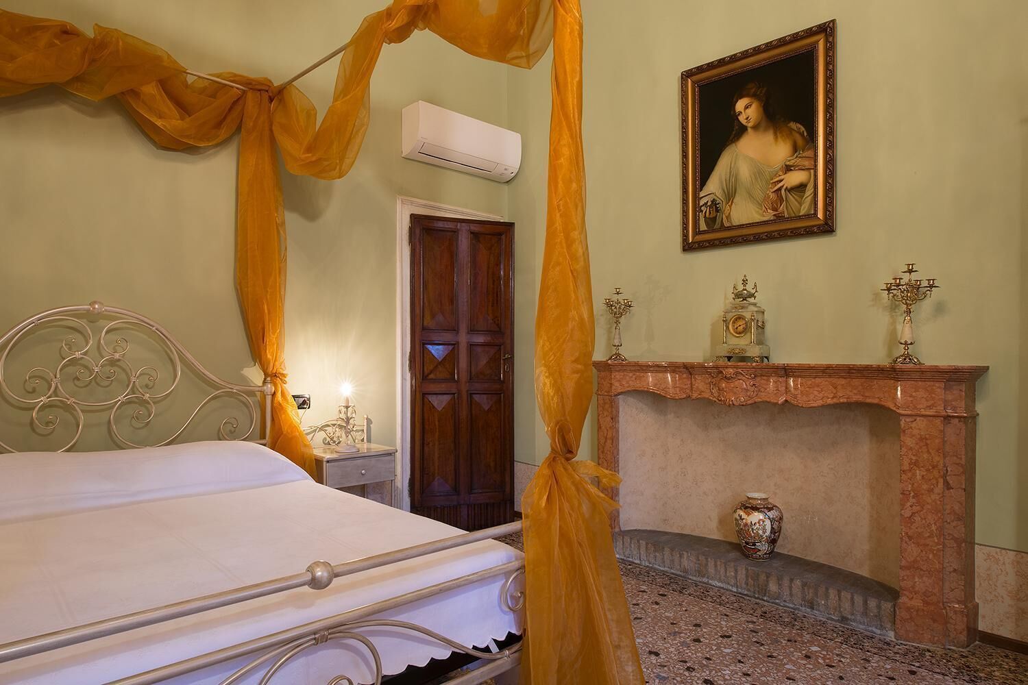 A bedroom with a bed, a fireplace, a painting, and a door.