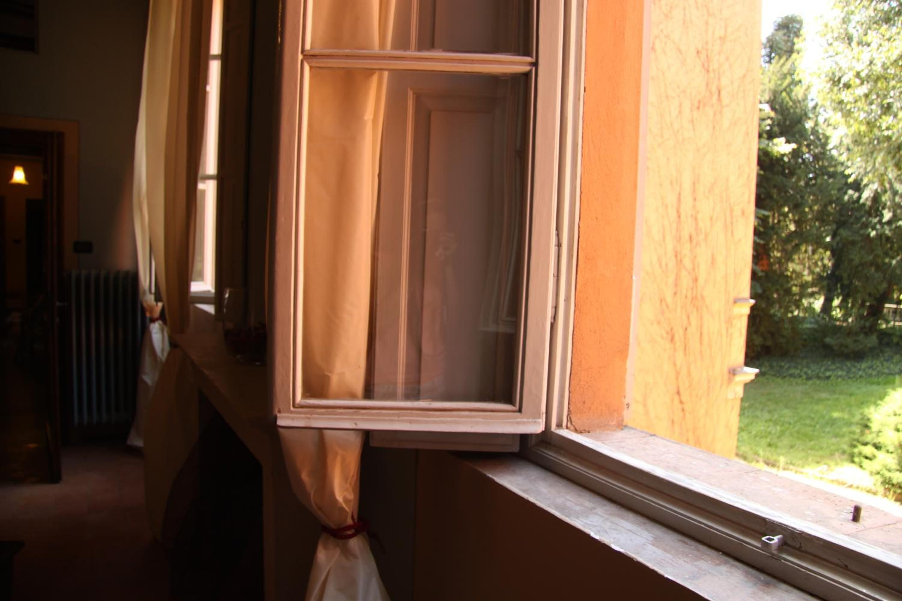 Una ventana con cortina entreabierta, mostrando una vista de un jardín.