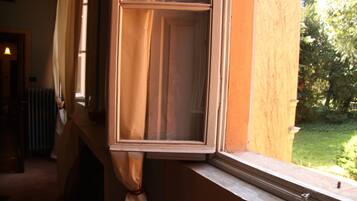 Una ventana con cortina entreabierta, mostrando una vista de un jardín.
