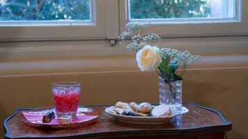 A table with a glass of pink drink, a plate of pastries, and a vase with flowers by a window.
