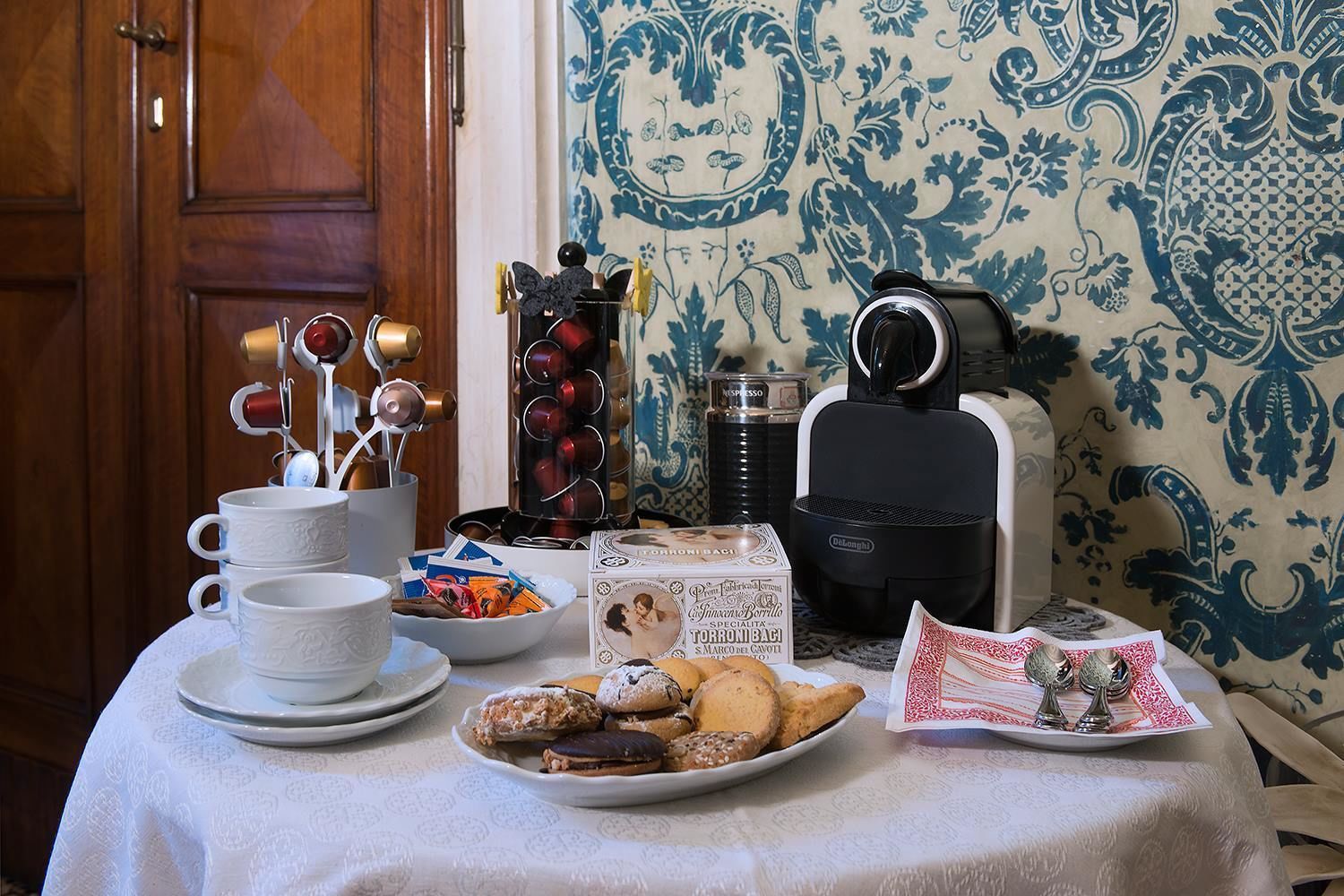 A table with a coffee maker, cups, a plate of pastries, a coffee grinder, and a decorative item.