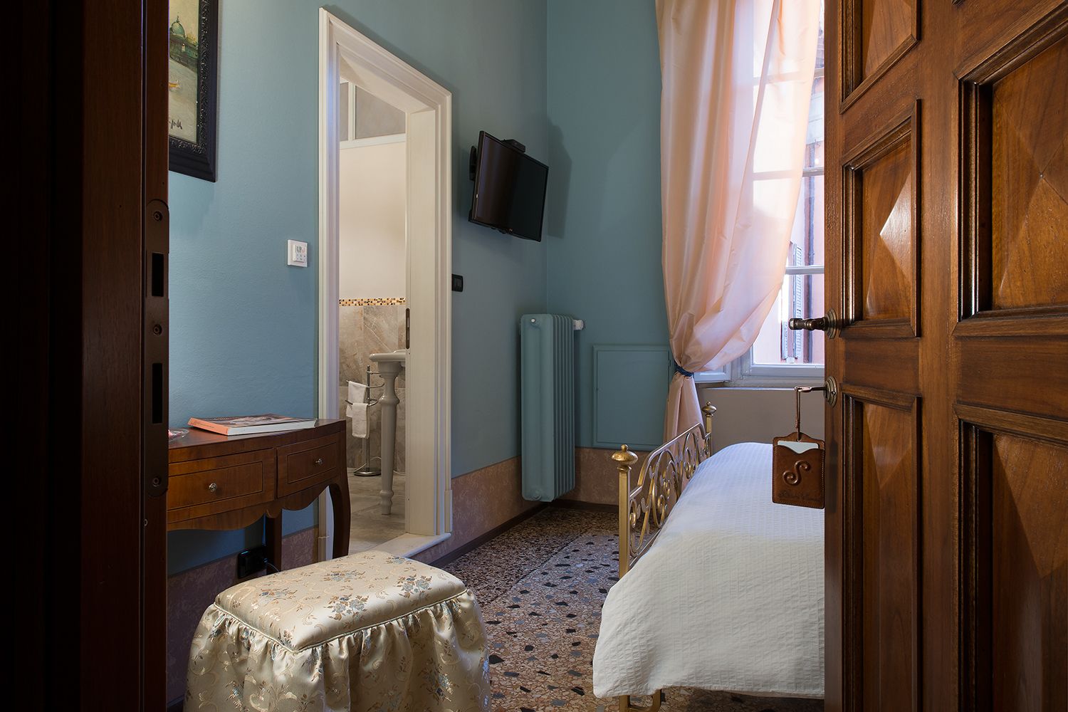 A bedroom with a bed, a desk, a chair, a television, and a window with curtains.