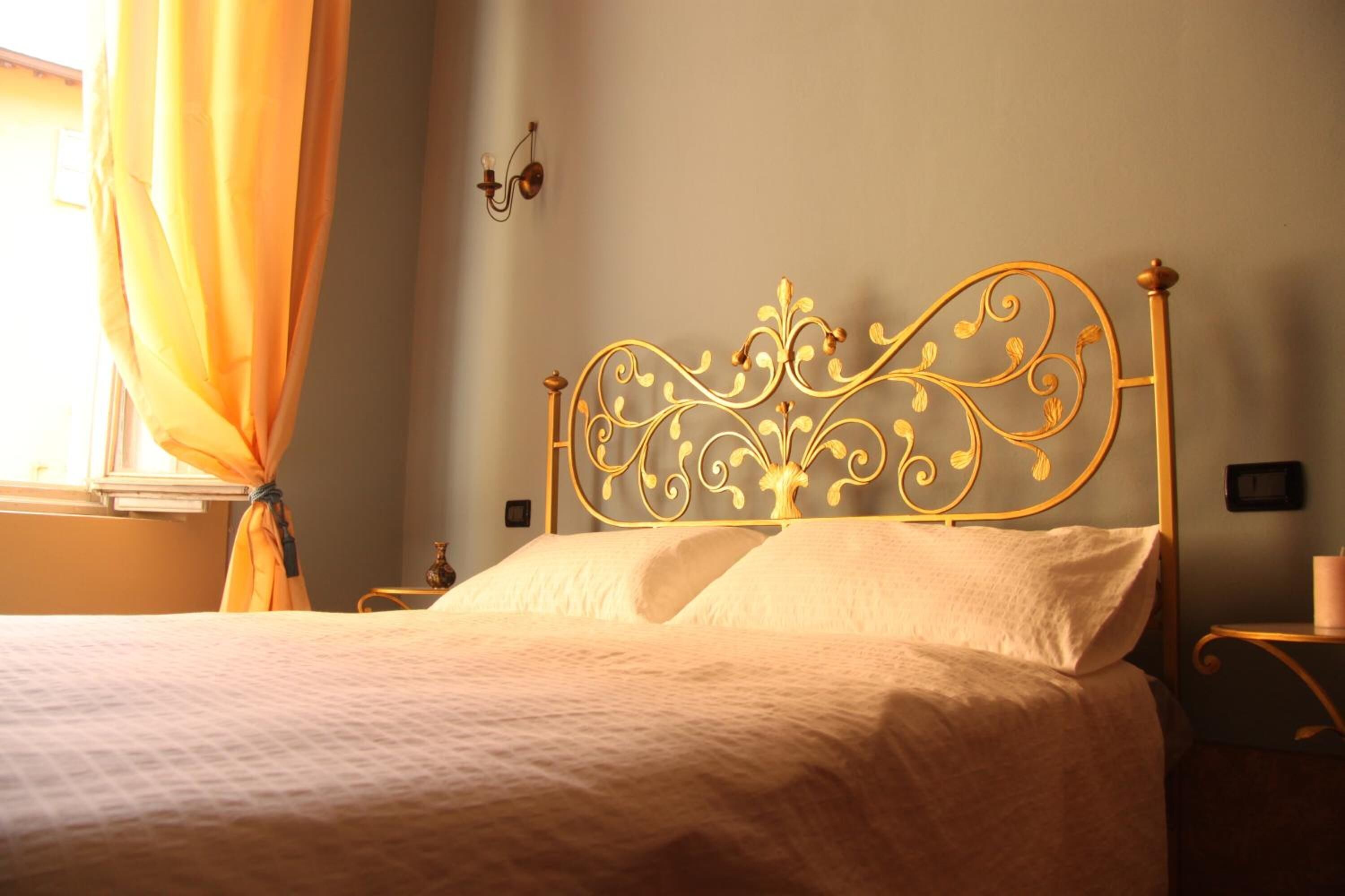 Una cama bien tendida con un cabecero metálico decorativo, una mesita de noche y una lámpara de pared.