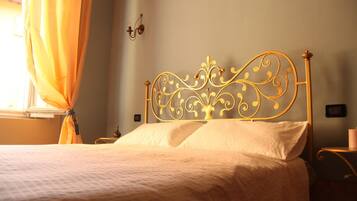 Una cama bien tendida con un cabecero metálico decorativo, una mesita de noche y una lámpara de pared.