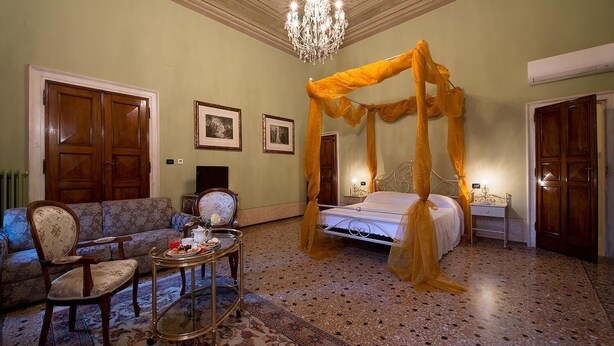 A room with a four-poster bed, a sofa, a small table with a tray of pastries, and a chandelier. - Salotto delle Arti (Modena)