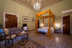 A room with a four-poster bed, a sofa, a small table with a tray of pastries, and a chandelier. - Salotto delle Arti (Modena)