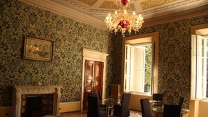 A room with patterned wallpaper, a fireplace, a chandelier, and a dining area with chairs and a table. - Salotto delle Arti (Modena)