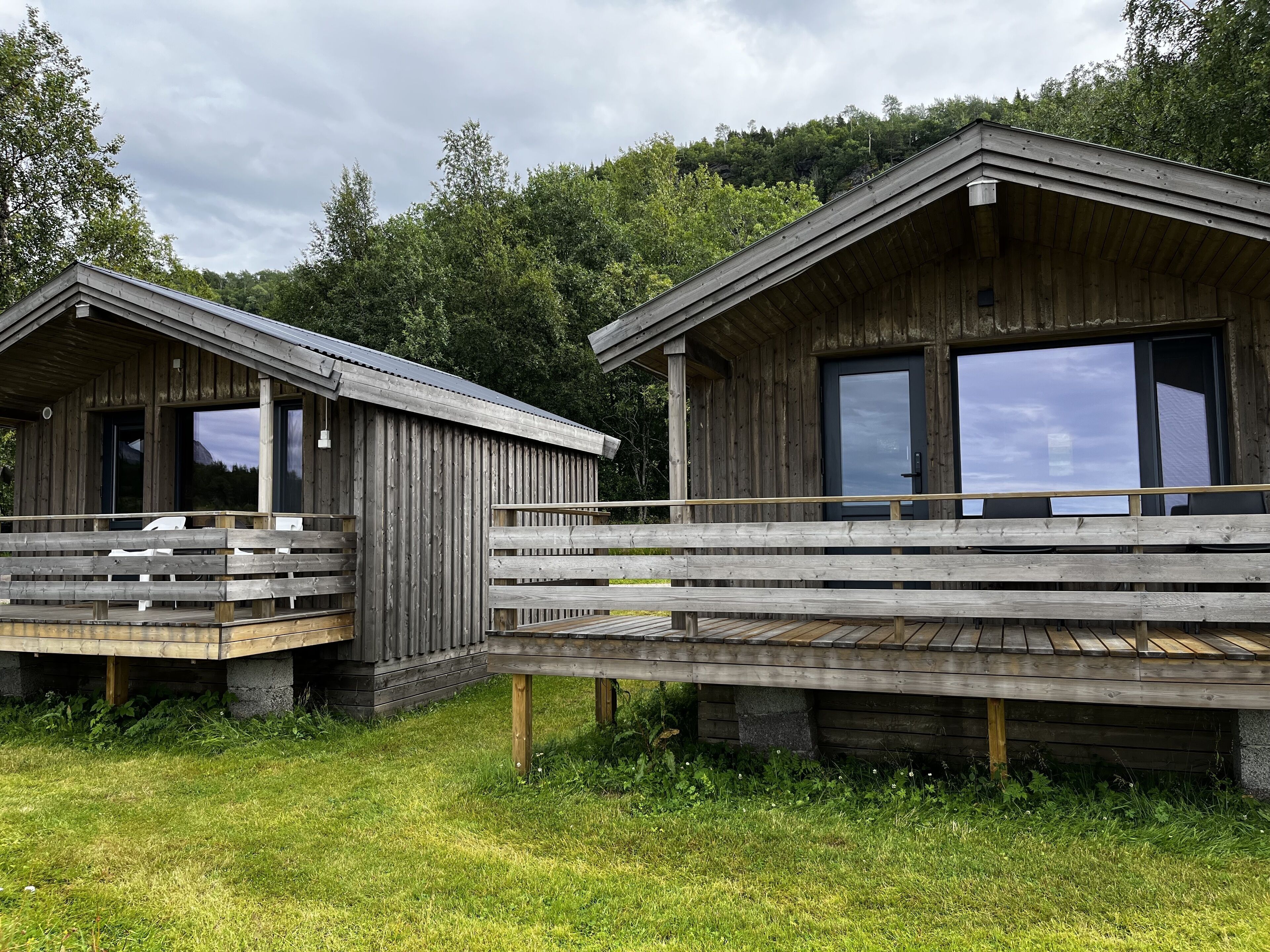 To træhytter med balkoner, en træterrasse der forbinder dem, og en skov i baggrunden.
